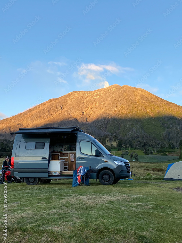 AdobeStock_1225930850_Preview A camper van parked on grass with its side door open, camping gear set up outside, and a mountain lit by sunlight in the background Specialized RV Repair and Conversions, Inc