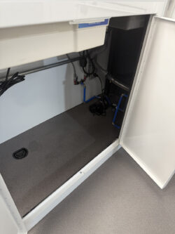 sprinter-conversions_0001_IMG_0703 Open white cabinet revealing a carpeted interior with visible pipes, cables, and plumbing fixtures installed along the walls and floor. Specialized RV Repair and Conversions, Inc.