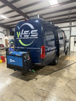 sprinter-conversions_0012_Layer 0 A blue W.E.S. rental and equipment solutions van is parked inside a warehouse with a Miller Bobcat machine mounted on its rear. Specialized RV Repair and Conversions, Inc.